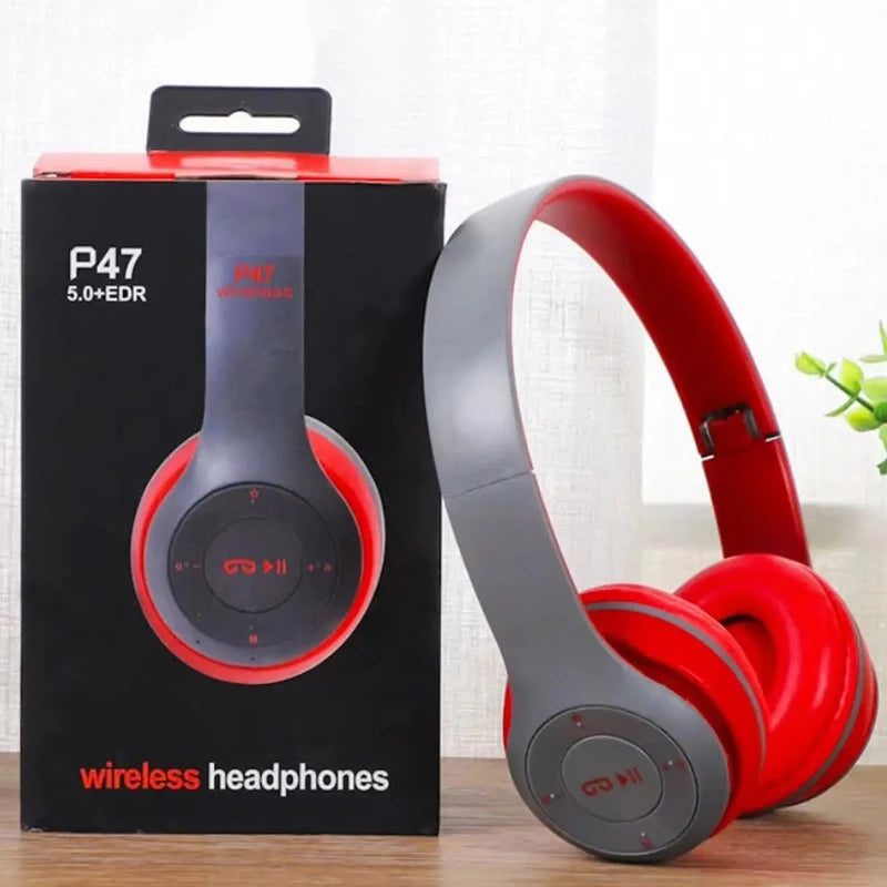 Red and gray wireless headphones next to their packaging box on a wooden surface.